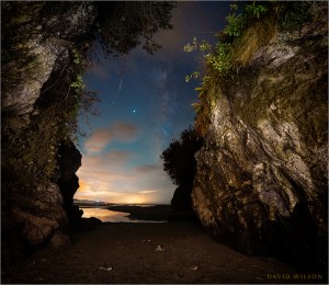 View out of a cave opening onto nighttime beach with Milky Way and stars