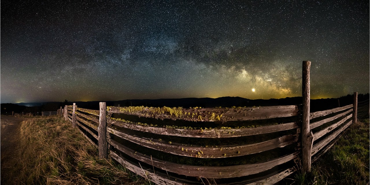 The Milky Way arches across the sky above an old ranch-style fence