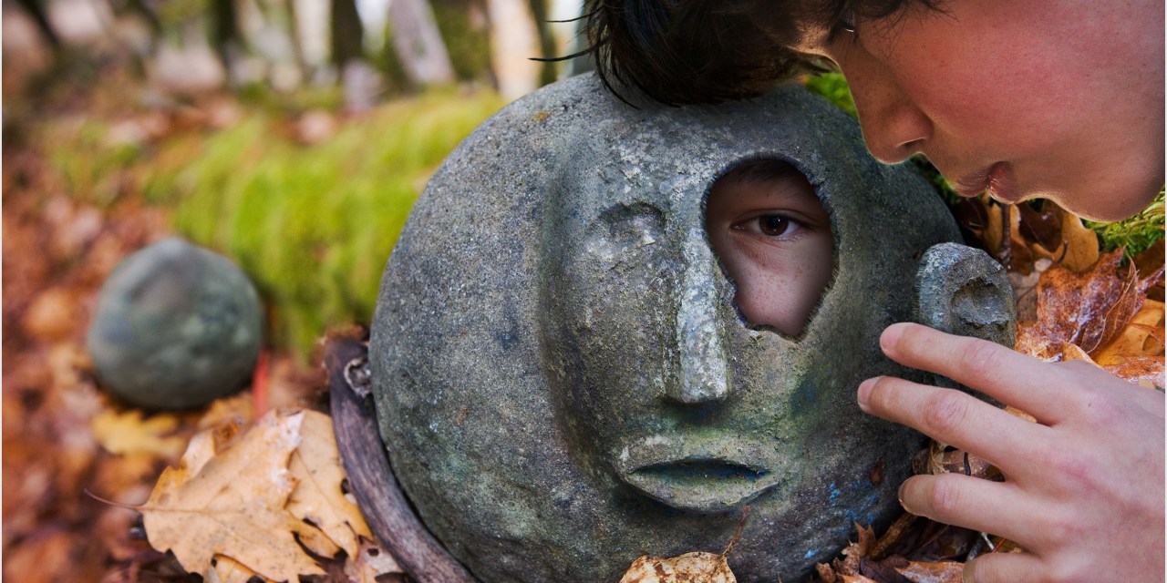 Digital photo montage of a boy finding a face within a rock. Not AI.
